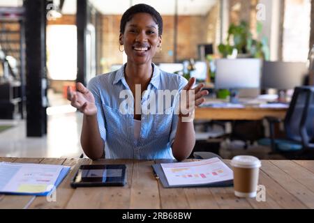 Portrait of happy african american casual businesswoman having video call and gesturing in office. Business, technology and work, unaltered. Stock Photo