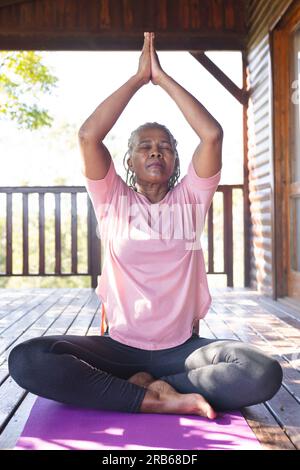 Focused senior african american woman practicing yoga on mat on terrace. Senior lifestyle, relaxing, retirement, healthy life, fitness, exercise and w Stock Photo