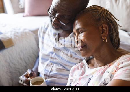 Thoughtful senior african american couple sitting on floor and drinking coffee at home. Senior lifestyle, relaxing and retirement, unaltered. Stock Photo