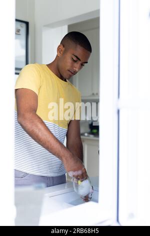 Biracial man doing washing up in kitchen sink. Healthy lifestyle, chores, cleaning and domestic life, unaltered. Stock Photo