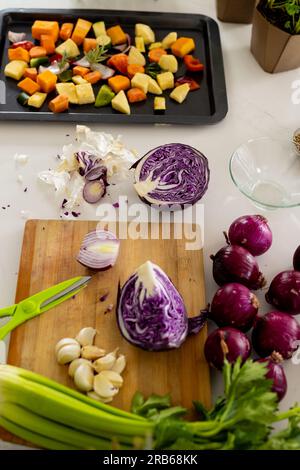 Vegetables on chopping board and chopped vegetables in baking tray on worktop in sunny kitchen. Cooking, food, ingredients, healthy living and domesti Stock Photo