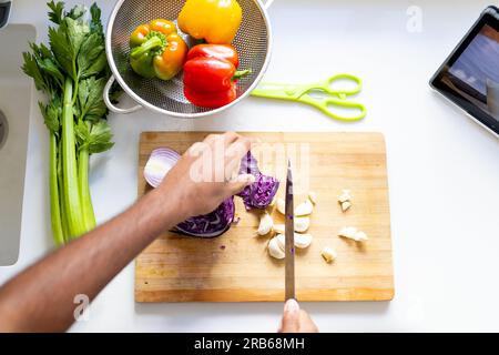 Hands of biracial man chopping vegetables and using tablet in sunny kitchen. Cooking, food, communication, recipe, healthy living and domestic life, u Stock Photo