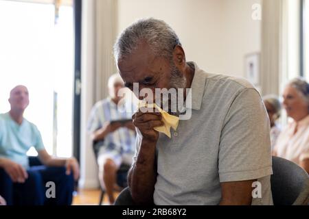 Distressed senior biracial man holding tissue and crying in group therapy session. Senior lifestyle, friendship and support, retirement, unaltered. Stock Photo