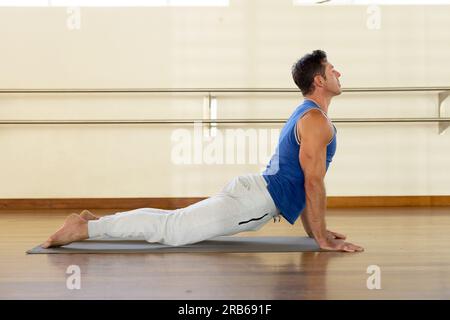 Caucasian man practicing yoga on mat in studio. Healthy lifestyle, wellbeing, yoga, fitness and exercise, unaltered. Stock Photo