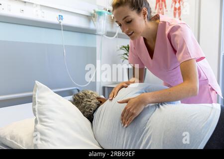 Diverse female doctor and senior female patient examining back at hospital. Hospital, medicine and healthcare services, unaltered. Stock Photo