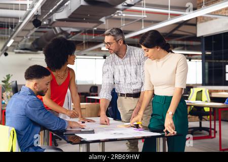 Diverse casual business people looking at architectural plans and discussing work at office. Business, teamwork, architecture and design. Stock Photo