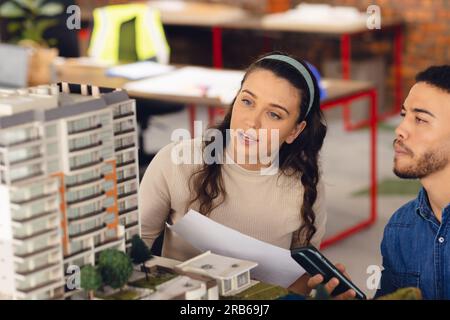Diverse business people looking at architectural model and discussing work at office. Business, teamwork, architecture and design. Stock Photo