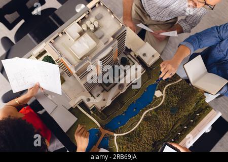 Diverse business people looking at architectural plans and model, discussing work at office. Casual business, teamwork, architecture and design, unalt Stock Photo