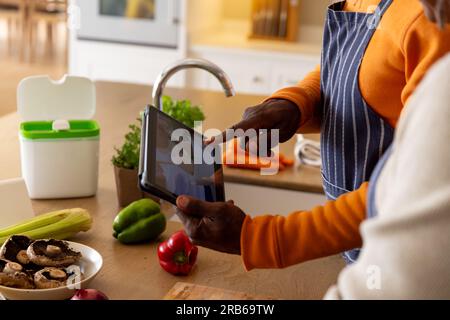 Midsection african american senior preparing vegetables and using tablet in kitchen. Senior lifestyle, food, cooking, communication, retirement, toget Stock Photo