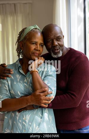 Thoughtful african american senior couple embracing and talking, looking out of window. Senior lifestyle, retirement, togetherness and domestic life, Stock Photo
