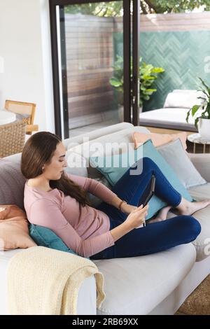 Caucasian woman using tablet on couch with copy space at home. Domestic life, technology and lifestyle, unaltered. Stock Photo