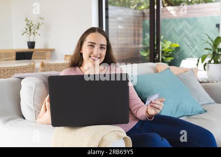 Portrait of happy caucasian woman using laptop and holding credit card. Domestic life, shopping, technology and lifestyle, unaltered. Stock Photo