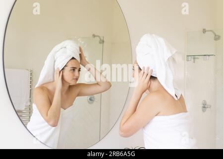 Caucasian woman with towel on head touching her face in bathroom. Domestic life, selfcare and lifestyle, unaltered. Stock Photo