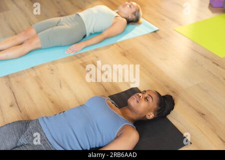 Diverse women relaxing with eyes closed, practicing yoga on mats in studio. Unaltered, yoga, exercise, fitness and healthy lifestyle. Stock Photo