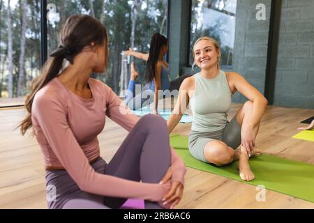 Happy diverse women practicing yoga on mats in studio. Unaltered, yoga, exercise, fitness and healthy lifestyle. Stock Photo