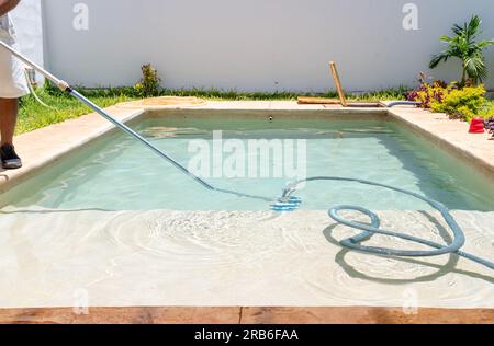 Latin man cleaning a garden pool with a vacuum cleaner. Stock Photo