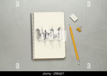 Sketch of cityscape in notebook, pencil and eraser on grey table, flat lay Stock Photo