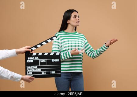 Actress performing while second assistant camera holding clapperboard on beige background. Film industry Stock Photo