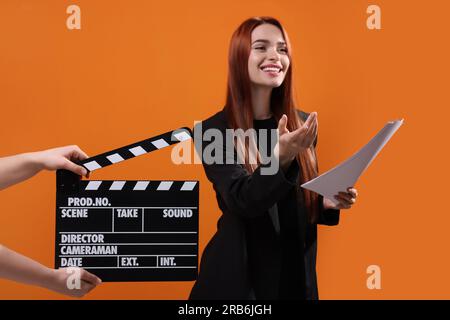 Actress performing role while second assistant camera holding clapperboard on orange background, selective focus Stock Photo