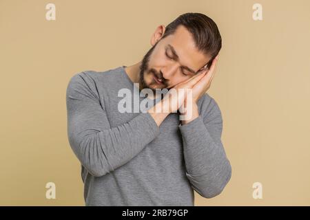 Tired overworked young lebanese man yawning sleepy inattentive feeling somnolent lazy bored gaping suffering from lack of sleep. Exhausted middle eastern guy isolated on studio beige background indoor Stock Photo
