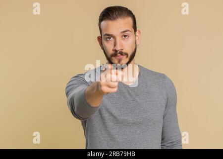 Quarrel. Displeased young lebanese man gesturing hands with irritation and displeasure, blaming scolding for failure, asking why this happened. Middle eastern guy isolated on beige studio background Stock Photo
