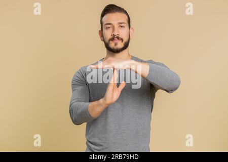 Tired serious upset young lebanese man showing time out gesture, limit or stop sign, no pressure, I need more time, relax, break deadline. Middle eastern guy isolated on studio beige background indoor Stock Photo
