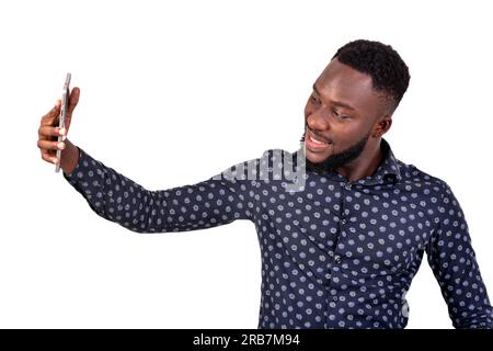 a young bearded man standing on a white background self-photographing using cell phone, smiling. Stock Photo