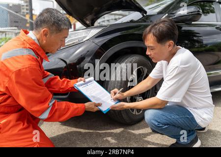 A car insurance agent showing the male customer where to sign the car insurance claim form, both sitting next to the car Stock Photo