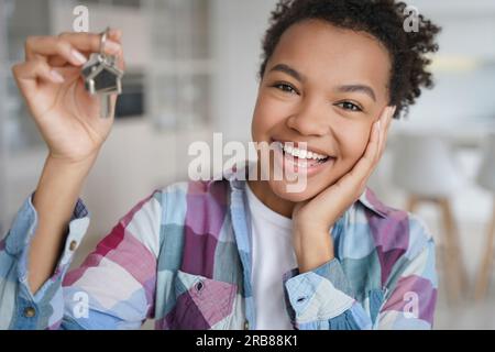 Delighted biracial teen tenant proudly displays keys to new home, embracing independence from parents. Stock Photo