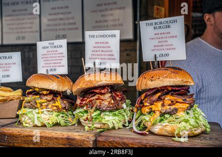 Beef burgers with cheese, bacon, lettuce, onions and pickles on sale at a street food stall in a local farmer market Borough Market in London . Stock Photo