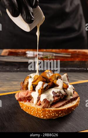 Cook preparing burger adding the sauce. The process of making a burger. Stock Photo