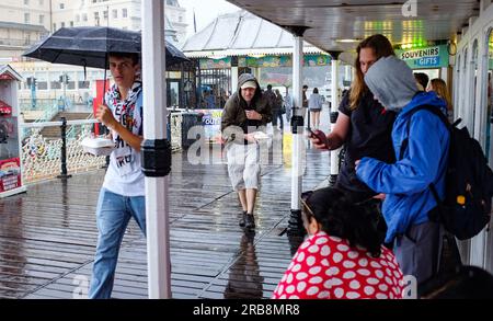 Brighton UK 8th July 2023 - Visitors make a dash for it as they try to escape the torrential rain showers on Brighton Pier as thunder storms sweep across parts of the UK today  : Credit Simon Dack / Alamy Live News Stock Photo