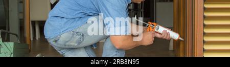 Image of the hands of a handyman who with a silicone gun installs and seals doors and windows against drafts. Home thermal insulation improvements. Stock Photo