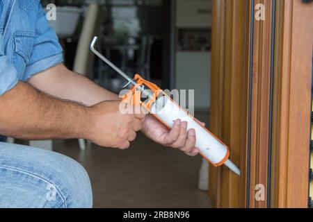 Image of the hands of a handyman who with a silicone gun installs and seals doors and windows against drafts. Home thermal insulation improvements. Stock Photo