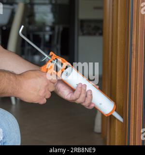 Image of the hands of a handyman who with a silicone gun installs and seals doors and windows against drafts. Home thermal insulation improvements. Stock Photo