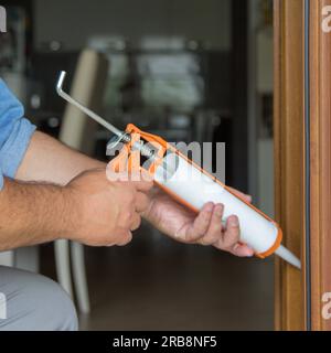 Image of the hands of a handyman who with a silicone gun installs and seals doors and windows against drafts. Home thermal insulation improvements. Stock Photo