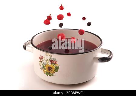 various berries fall into compote, isolate on white, pot with hot drink Stock Photo