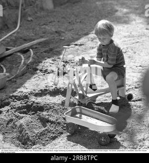 In the 1960s. A boy is playing with a toy excavator, digs up sand and dumps it int he plastic carriage. A common toy in the 1960s. Sweden June 1966 Stock Photo