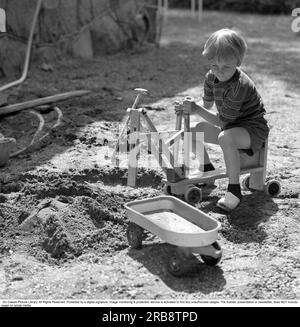 In the 1960s. A boy is playing with a toy excavator, digs up sand and dumps it int he plastic carriage. A common toy in the 1960s. Sweden June 1966 Stock Photo