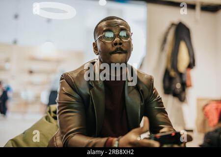 Young excited man sitting on sofa playing video games using remote control joystick with freak intense face expression having fun in gaming addiction Stock Photo