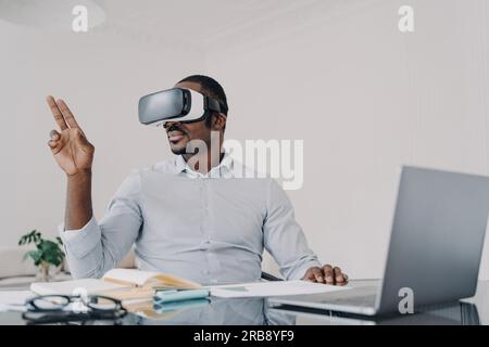 African american businessman wearing vr glasses working on project in cyberspace at laptop. Black male manager works in augmented virtual reality, usi Stock Photo