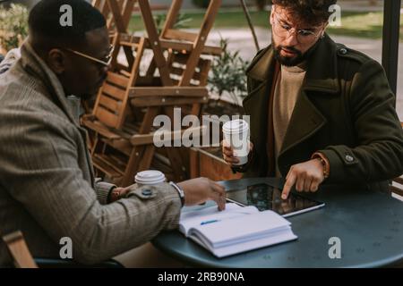 Business talk between to diverse partners. White man showing something on the tablet to his black colleague Stock Photo