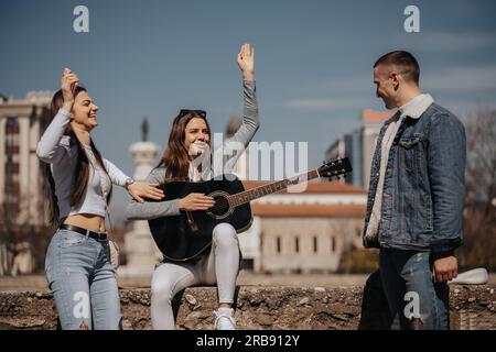 Three best friends having fun while playing guitar and singing outside Stock Photo