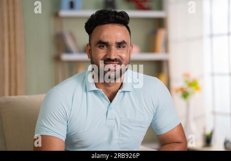 Happy smiling man looking at camera while sitting on sofa at home - concept of successful, satisfaction and relaxation Stock Photo