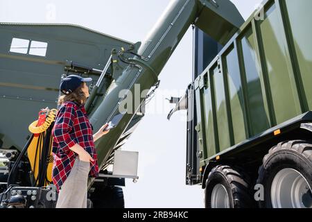 Woman farmer with tablet watching grain loading. Stock Photo