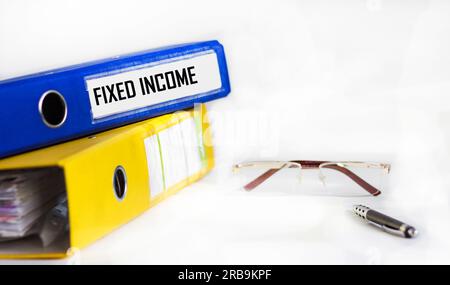 FIXED INCOME text on blue folder with pen, glasses on white background Stock Photo