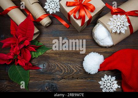 The concept of preparing for the Christmas holiday. Flatley. View from above. On a wooden table there are items for preparing for Christmas - a stollen, wrapping paper for gifts, a gift, a Santa hat, pointessia Stock Photo