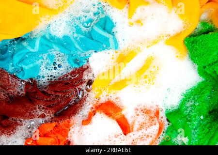 Colored clothes soaked in water with detergent and foam bubbles. Washing by hand. Stock Photo