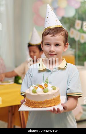 Portrait of preteen boy in party hat carrying birthday cake Stock Photo