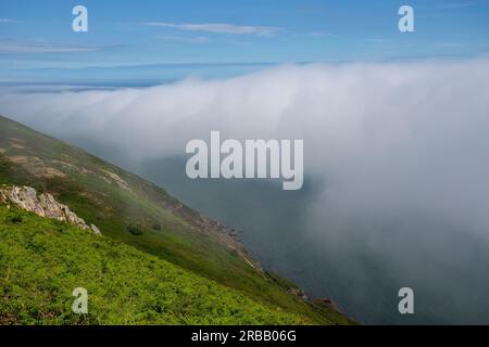 View from the summit of Bray Head with sea mist rolling over the coastline Stock Photo